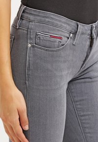 Vaqueros de denim gris con un corte ajustado, que presentan un pequeño bolsillo frontal con rayas de acento en rojo, blanco y azul, y sutiles detalles de costura.