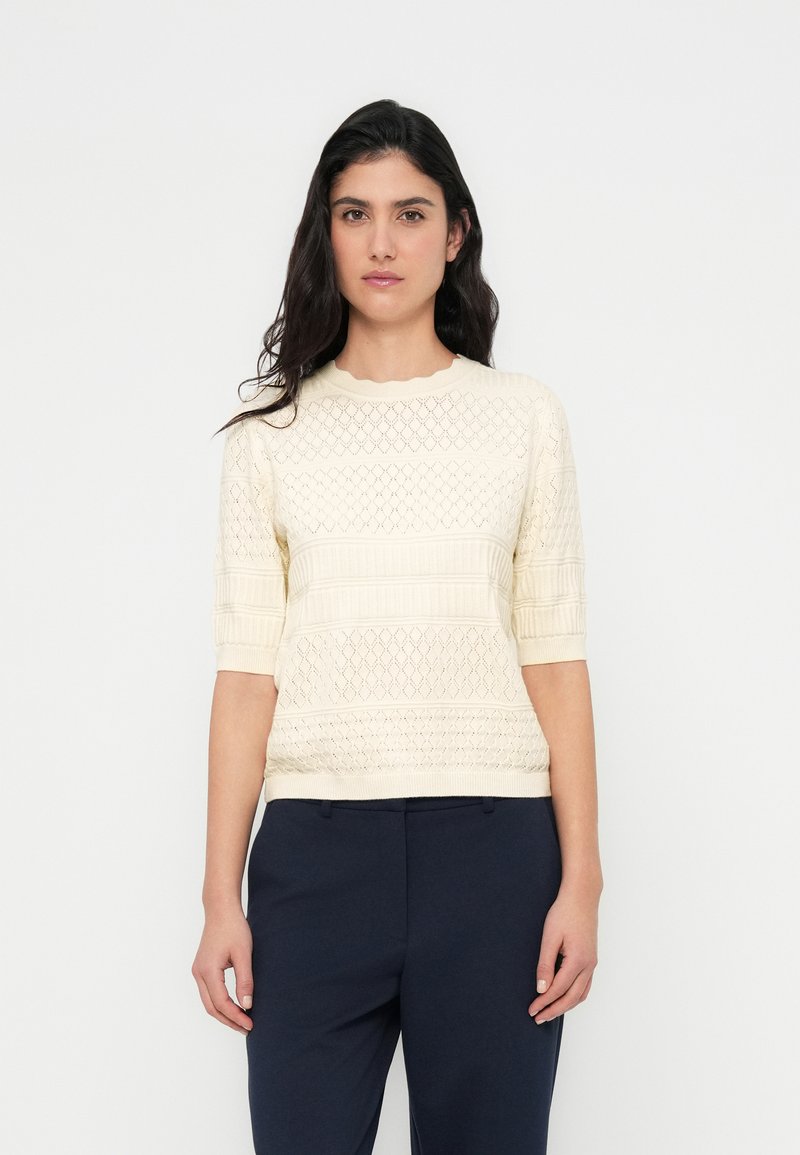 Ελαφρύ κρεμ πλεκτό πουλόβερ με κοντά μανίκια, με ανοιχτά διαμαντένια σχέδια και ριμπ λεπτομέρειες στο ντεκολτέ και το τελείωμα.