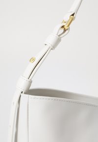 Weiße Lederhandtasche mit einer glatten Textur, die mit goldfarbenen Hardware-Details verziert ist und über einen verstellbaren Riemen für Vielseitigkeit in der Nutzung verfügt.