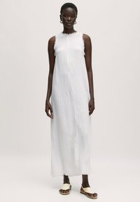 Weißes Leinen-Maxi-Kleid mit geradem Schnitt, fransigen Kanten und Rundhalsausschnitt. Kombiniert mit leichten, minimalistischen Rutsch-Sandalen.