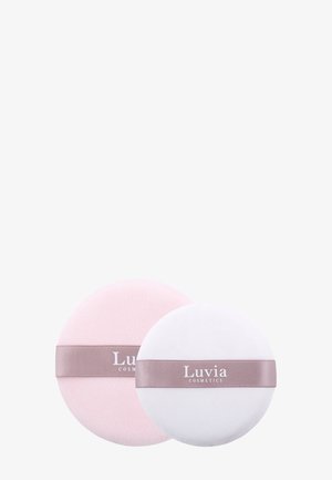 Deux applicateurs cosmétiques ronds en rose pastel et blanc. Chacun présente une texture lisse et un ruban satiné avec l'inscription « Luvia Cosmetics ».