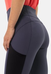Leggings taille haute en tissu bleu marine foncé avec une poche latérale noire, présentant des coutures contrastantes et une texture lisse. Ajustement amélioré au niveau de la taille et des hanches.