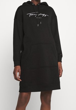 Czarna sukienka z kapturem i długimi rękawami, z kieszenią z przodu, sznurkami i białym logo "Tommy Hilfiger est. 1985" na piersi.