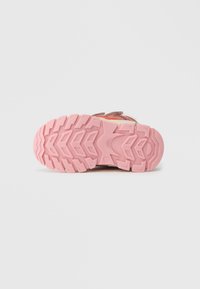 Rosa gummisula p å ett barns sneakers med djupa mönster, fotograferad från undersidan mot en enfärgad vit bakgrund.