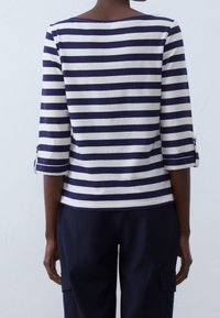 Mörkblå och vit randig topp med trekvartsärmar, med rullade manschetter som åtsätts med knappar, tillverkad av mjukt och lätt tyg.