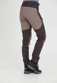 Dames buitenbroek in donkerbruin en zandkleur, gemaakt van duurzaam materiaal, met een aansluitend ontwerp, een ritszak en een versterkt enkelgebied.