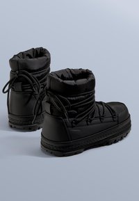 Černé zateplené boty mají polstrovaný lem, šněrování, texturovanou gumovou podrážku a elegantní voděodolný syntetický materiál.