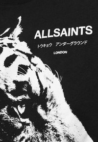 Camiseta negra con un gráfico de tigre blanco, texto "ALLSAINTS" y letras japonesas adicionales. Material de algodón con una textura suave.