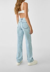 Jeans de tiro alto en azul claro con pierna recta, bolsillos traseros y dobladillo sin acabar, hechos de tela de mezclilla con una textura ligeramente desgastada.