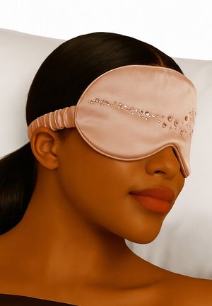 Jedwabna maska na oczy w delikatnym brzoskwiniowym kolorze z elastycznym paskiem, z ozdobną linią małych, przejrzystych kryształków na przodzie.