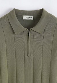 Polo shirt en maille c�ôtelée vert olive avec zip half et col évasé, taille M.