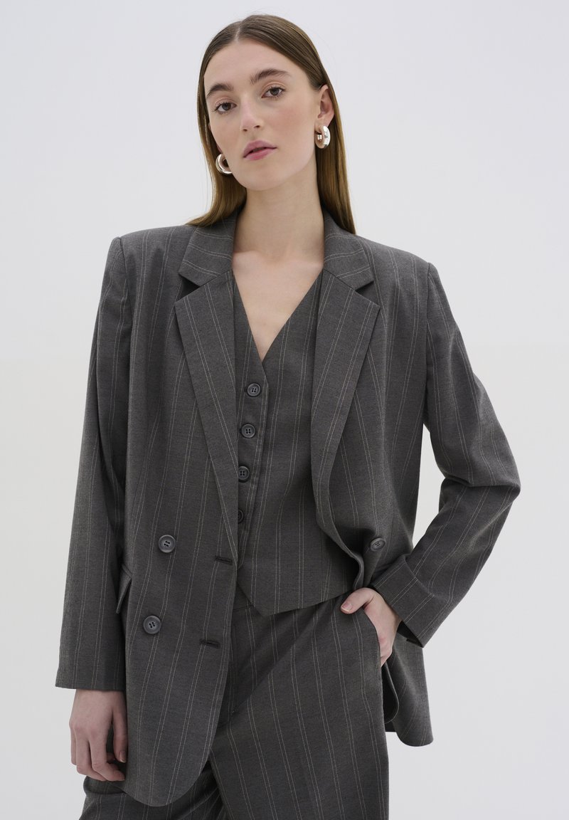 Blazer grigio a righe con rever a punta e chiusura a doppio bottone, abbinato a un gilet coordinato con scollo a V e dettagli con bottoni.