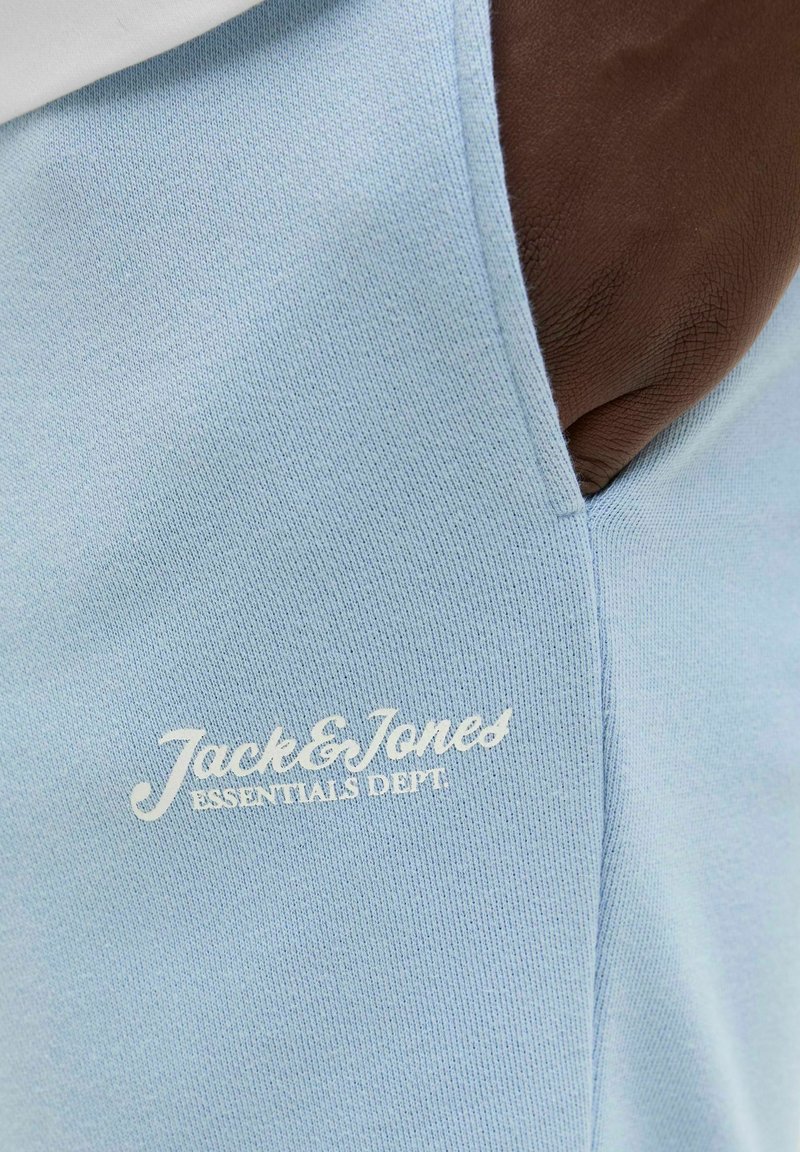 Svijetloplava tkanina s glatkom teksturom, s bijelim izvezenim natpisom "Jack & Jones ESSENTIALS DEPT" na prednjoj strani.