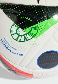 Replika zápasovej lopty s bielym povrchom a čiernymi, zelenými a červenými akcentmi. Obsahuje bodkované vzory a potlač textu pre pamätihodnosti.