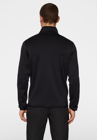 Svart fleecetröja, hög krage, långa ärmar, slät textur och inga synliga logotyper eller mönster. Lämplig för vardagsbruk eller lager-på-lager.