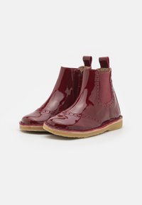 Botas de tobillo de charol rojo con paneles elásticos laterales, punta redonda y suela de goma marrón. Presenta un detalle de costura en la parte superior.