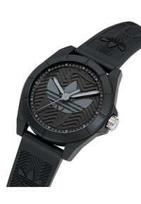 Montre analogique noire avec un cadran noir texturé, des accents gris et un bracelet en caoutchouc présentant un motif subtil. Détails de couronne argentée.