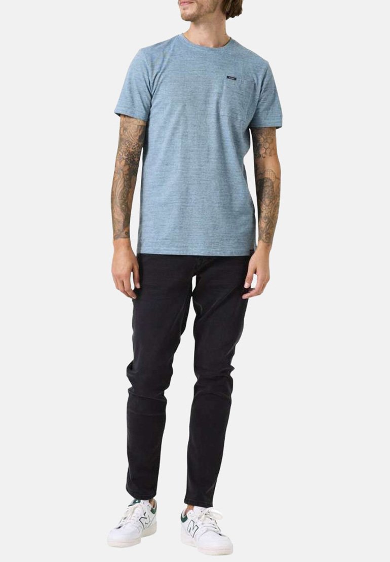 Camiseta corta de manga azul con textura y cuello redondo, combinada con pantalones negros y zapatillas blancas, con un pequeño logo en el pecho.