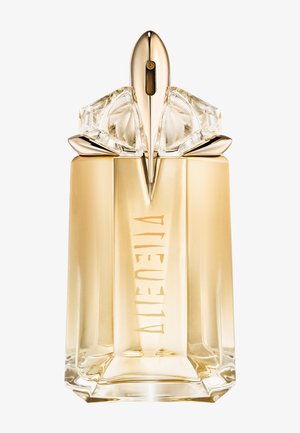 Flacon de parfum en verre clair et doré avec un design géométrique, présentant un bouchon facetté et un logo en relief sur le devant.