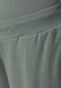 Soft, stretchy fabric in muted green; features a wide waistband and gentle pleats, emphasizing comfort and easy wear.