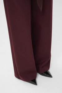 Burgundy wide-leg trousers paired with black patent pointed-toe heels. The fabric appears smooth with a slight sheen.