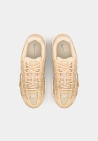 Baskets Nike beiges avec des panneaux en mesh, un système de laçage et des accents gris subtils. Bout rond et semelle en caoutchouc texturée.