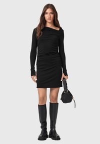 Abito lungo nero a maniche lunghe con design arricciato, scollo off-the-shoulder, abbinato a stivali neri al ginocchio e una piccola borsa nera.