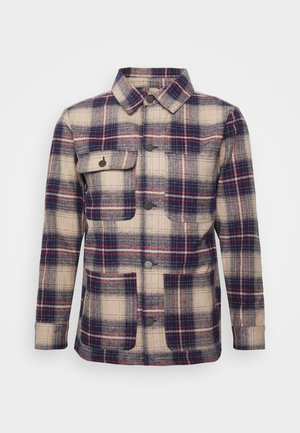 Veste à boutons à carreaux beige, marine et rouge avec col, manches longues, une poche à rabat sur la poitrine et deux poches plaquées à l'avant.