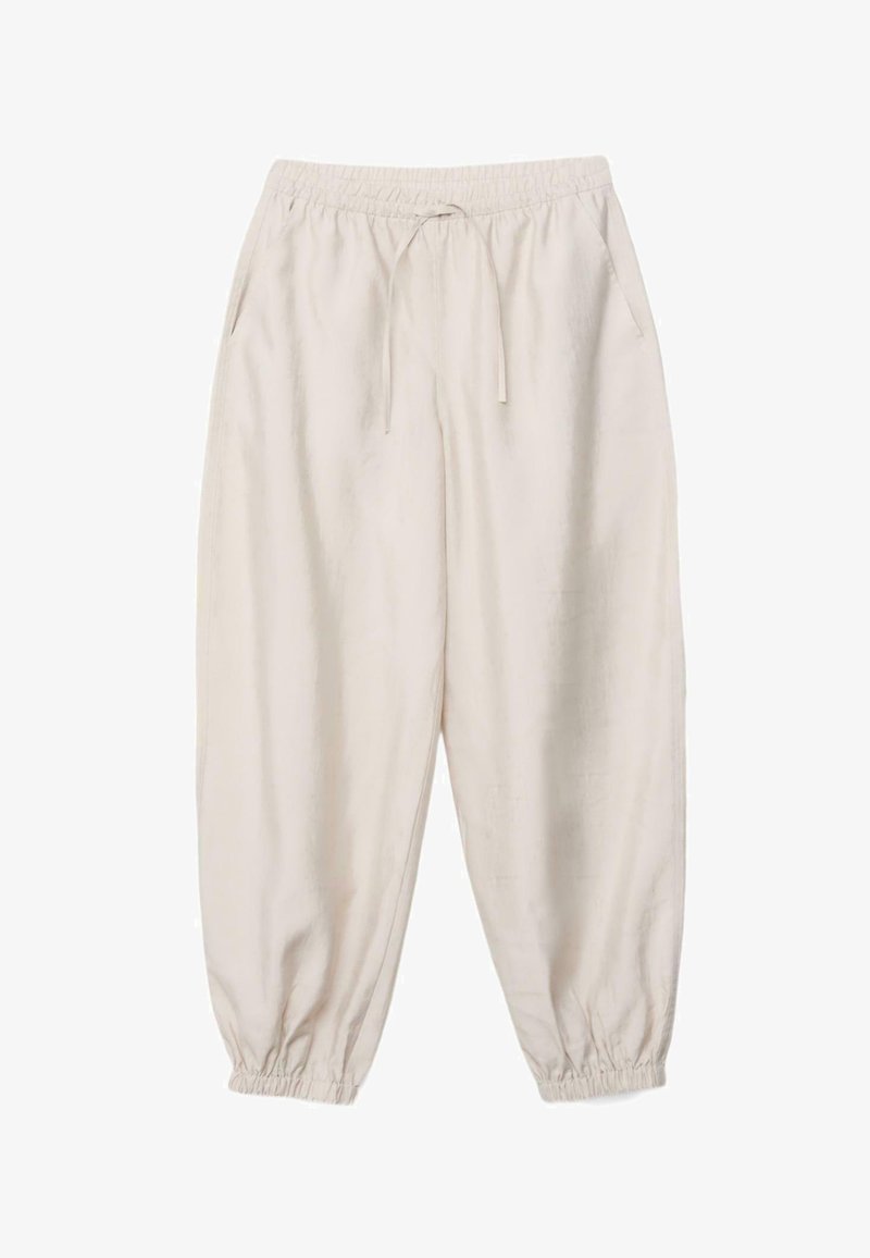 Luźne spodnie w jasnobeżowym kolorze, z elastycznym pasem, sznurkiem do ściągania, bocznymi kieszeniami oraz elastycznymi mankietami przy kostkach.