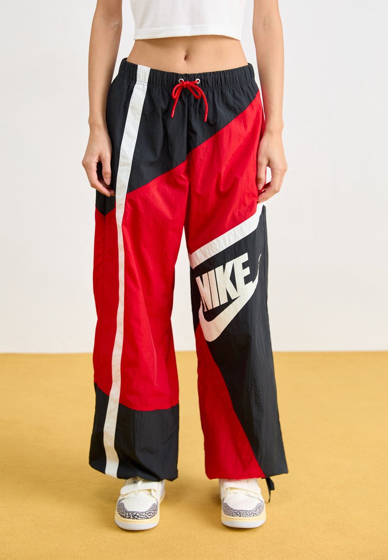 Piros és fekete nylon nadrág, fehér díszítéssel, húzózsinórral a derekán és nagy Nike logóval az alsó lábszáron. Széles lábak, könnyű textúra.