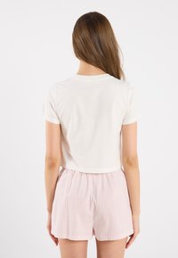 Skraćeni bijeli T-shirt s kratkim rukavima u kombinaciji s laganim kratkim hlačama ružičastih prugica, prikazujući jednostavan dizajn i mekanu teksturu tkanine.