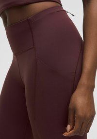 Bordó, magas derekú leggings sima, rugalmas anyagból, oldalsó zsebbel, lapos varratokkal és diszkrét cipzárral a derékrészen.