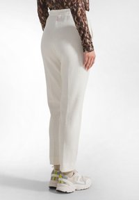 Witte textuurbroek met een losse pasvorm en elastische tailleband, met een cropped lengte en zijslits. Draagt met lichtgekleurde sneakers.