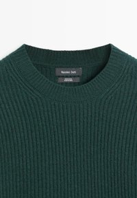 Dunkelgrüner, gerippter Wollpullover mit Rundhalsausschnitt. Das Etikett trägt die Aufschrift "Massimo Dutti" und weist darauf hin, dass er aus 100 % Wolle besteht. Glatte Textur.