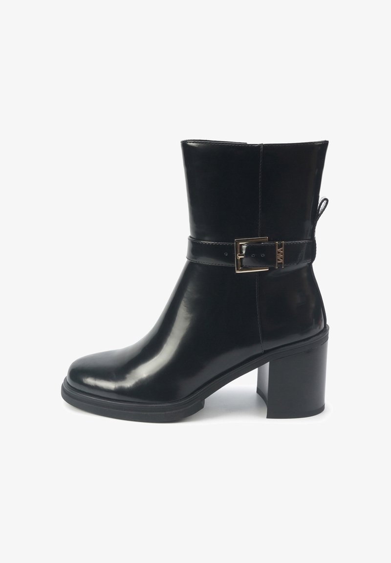 Bottine noire en matériau brillant, avec un bout rond, un talon épais, une boucle latérale et un détail de lanière. Texture lisse partout.