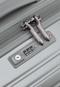 Valigia grigia con lucchetto a combinazione, maniglie a doppia zip e superficie testurizzata con un logo. Include un foro per la chiave per una maggiore sicurezza.