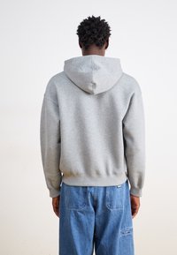 Haut à capuche gris avec cordon de serrage, poignets et ourlet côtelés, fabriqué en tissu doux, porté avec un pantalon en denim large bleu.