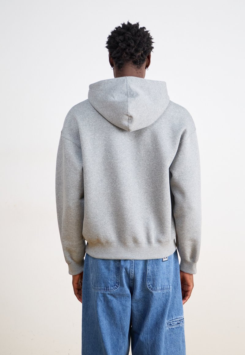 Grauer Kapuzenpullover mit Zugbändern, gerippten Bündchen und Saum, aus weichem Stoff, getragen mit blauen weiten Denim-Hosen.