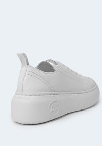 Baskets basses blanches avec semelle épaisse, languette au talon, logo embossé "AX" sur la semelle et détails cousus le long du côté.