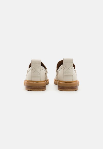 O pereche de loafers din piele off-white, cu tocuri din lemn stratificat de culoare tan, cu cusături vizibile și etichete de marcă la spate, prezentate din punct de vedere posterior.