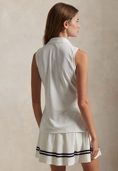 Λευκό αμάνικο πόλο πουκάμισο με κλασικό γιακά· φουστάνι με πιέτες σε στρώσεις σε λευκό χρώμα με ναυτικό ριγέ λεπτομέρειες στο τελείωμα.