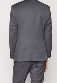 Grå kostym med en slät tygkvalitet, slim fit-design, en ventil på baksidan och knäppning vid ärmsluten. Skräddarsydda byxor synliga nedanför.