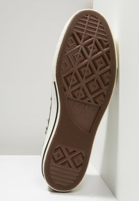 Trampki Converse All Star z chropowatą, brązową gumową podeszwą, ozdobioną wzorem diamentów, białą płócienną cholewką z czarnymi akcentami.