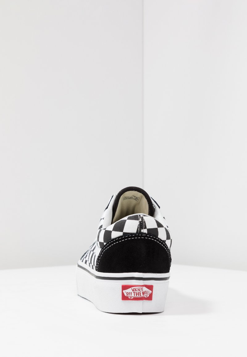Zapatillas de lona con patrón de tablero de ajedrez en blanco y negro, con un acento de ante, suela plana blanca y etiqueta roja "Vans Off The Wall" en el talón.
