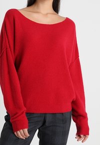 Röd överdimensionerad stickad tröja med vid halsringning, texturerad tyg och långa ärmar. Matchad med grå rutiga byxor.