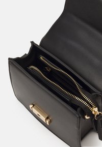 Mustassa nahkakengässä on kultainen lukko, ja sisällä on kaksi vetoketjullista osastoa. Pintakuvio on sileä ja muotoilu puhdas ja jäsennelty.