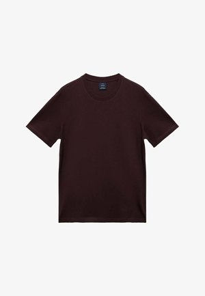 T-shirt cremoso marrone scuro a maniche corte con una piccola etichetta del marchio all'interno del colletto, posato su uno sfondo bianco.