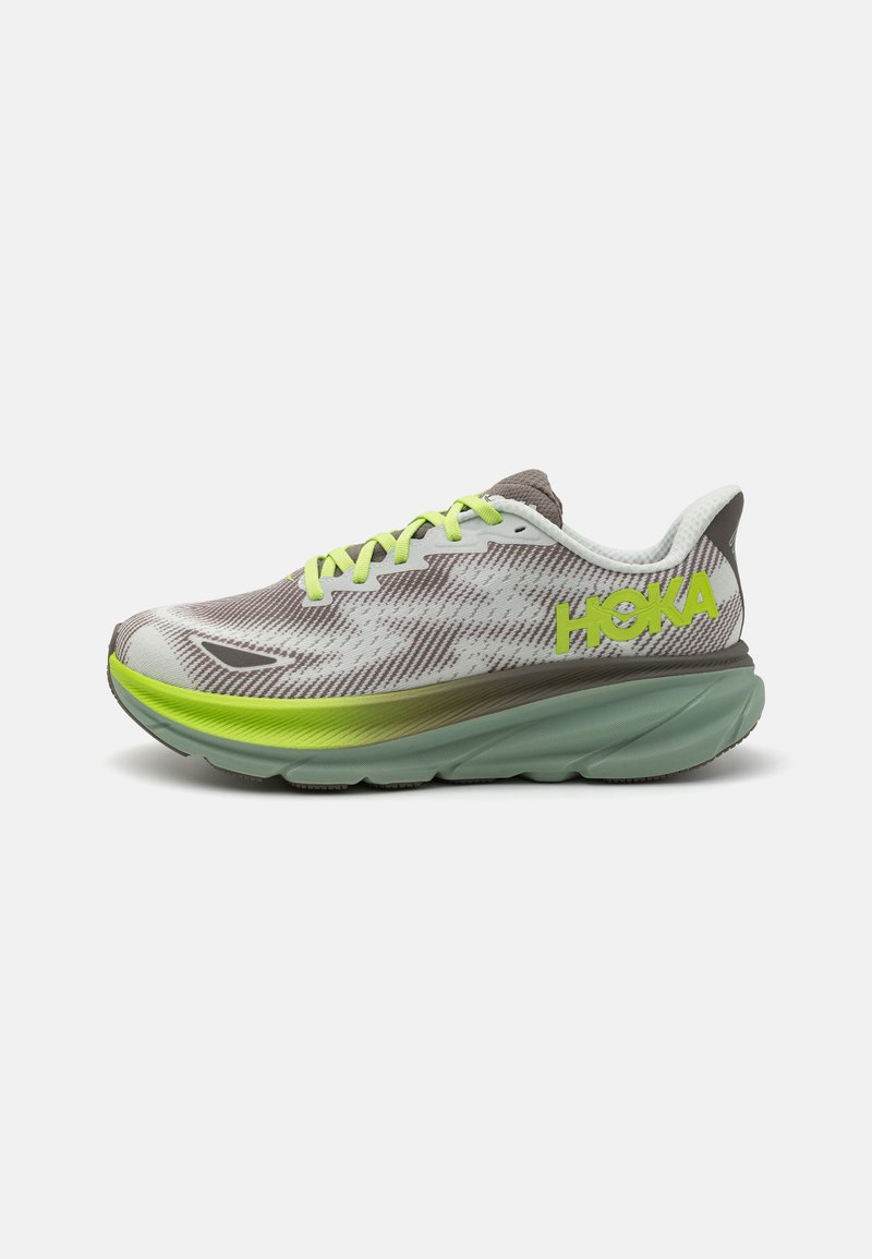 HOKA running shoe with a breathable mesh upper in gray and white, yellow-green laces, thick cushioned sole in light green, and textured pattern.