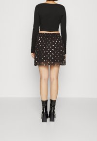 Svart långärmad crop top i kombination med en svart semi-transparent kjol med guldprickmönster, fulländad med kraftiga svarta klackstövlar.