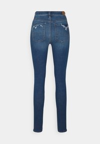 Jean skinny en denim bleu à taille haute, avec deux poches arrière et des détails usés sur le tissu. Ourlet net sans effilochage.